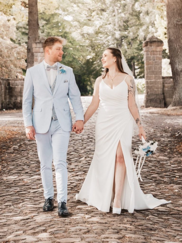 Paar in eleganter Hochzeitskleidung, umarmend am Wasser mit einer romantischen Atmosphäre.